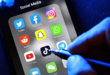 Social media apps on phone screen with hand holding stylus