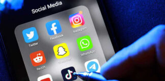 Social media apps on phone screen with hand holding stylus