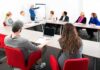 A diverse group of professionals engaged in a meeting with a presenter at a whiteboard
