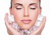 A woman with closed eyes holding ice cubes against her face