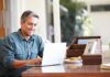 A man sitting at a desk working on a laptop with a smile