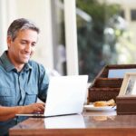 A man sitting at a desk working on a laptop with a smile