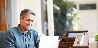 A man sitting at a desk working on a laptop with a smile