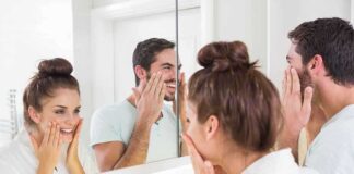 A couple smiling at their reflections in a bathroom mirror while applying skincare products