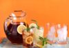 A pitcher of iced tea with lemon slices and mint, alongside glasses with ice and colorful straws