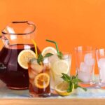A pitcher of iced tea with lemon slices and mint, alongside glasses with ice and colorful straws