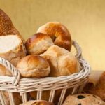 A basket filled with various types of fresh bread and rolls against a golden background
