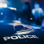 Marine Vet Shocks Nation in Deadly Officer Ambush Police car with blurred figures in the background.