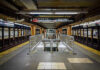 Subway station platform with directional signs overhead.