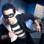 Bank Robber RETURNS–Dallas Branch Hit AGAIN A masked thief in a striped shirt holding a bag while emerging from a bank vault