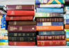 Several Bible editions stacked on a bookshelf.