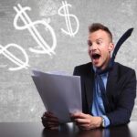 Excited businessman holding documents with dollar signs in the background
