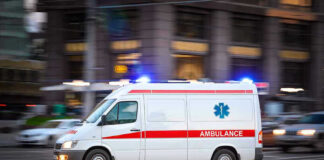 Ambulance driving on urban street with lights flashing.