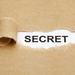 A torn piece of brown paper revealing the word SECRET underneath