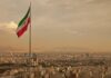Iranian flag waving over a city skyline with mountains in the background