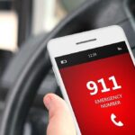 A smartphone displaying the emergency number 911 while held in a persons hand inside a car
