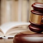 A wooden gavel resting on a sound block with law books in the background