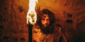 A prehistoric man holding a torch in front of cave paintings