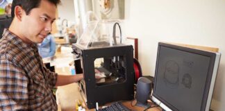 A person working at a desk with a 3D printer and computer