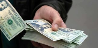 A hand holding a stack of hundred dollar bills with one bill prominently displayed