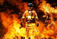 Firefighter standing in front of a large fire, equipped with tools
