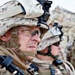 Two soldiers in military gear looking serious in an outdoor setting