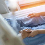 Hospital patient holding visitors hand reassuringly.
