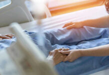 Hospital patient holding visitors hand reassuringly.