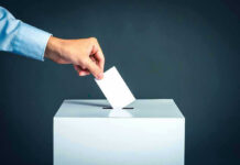 Hand placing ballot into voting box.