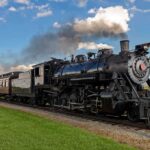Newsom’s Diesel Train LIE Caught on Camera A vintage steam locomotive pulling passenger cars on a railway track