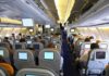 Interior view of an airplane with passengers seated and using in-flight entertainment screens