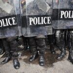 Police Raid Shocks James O’Keefe Police officers in riot gear standing behind shields marked POLICE