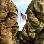 Massive U.S. Troop DEPLOYMENT Abruptly Canceled! Soldiers stand in formation with American flag in background.