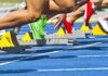 Athletes starting a sprint from starting blocks on a blue track