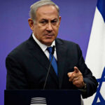 Leadership Rift Over Lebanon Campaign and Iran Policy Man in suit giving speech in front of Israeli flag.