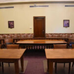 Parents Warned: UK Bill Could Turn Conversations Into Crimes Empty courtroom with wooden tables, chairs, and a door.