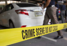 Crime scene tape blocking off white sedan.