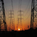 Amazon Deal Ties Indiana Jobs Boom to Energy Risk Transmission towers at sunset.