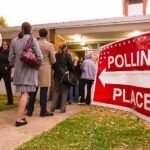 People waiting in line at a polling place with a sign indicating direction