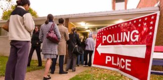 People waiting in line at a polling place with a sign indicating direction