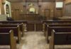 DOJ Backs Fired Coach in COVID Faith Fight Interior view of an empty courtroom with wooden benches and a judges bench