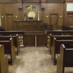 DOJ Backs Fired Coach in COVID Faith Fight Interior view of an empty courtroom with wooden benches and a judges bench