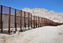 Feds Threaten Ranches: Open Gates Or Else A long border wall stretches across a desert landscape with mountains in the background