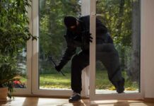 A burglar in dark clothing entering a house through a glass door