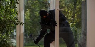 A burglar in dark clothing entering a house through a glass door