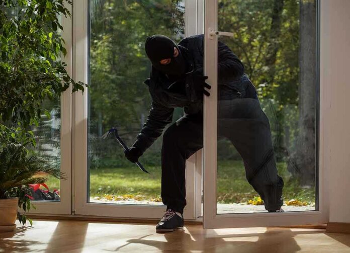 shutterstock_167973983 A burglar in dark clothing entering a house through a glass door