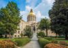 State capitol building with a gold dome surrounded by greenery and a statue
