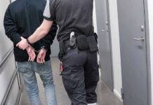 Evidence Blackout: Death Threat Suspect’s Trump Immunity Officer escorting handcuffed person down hallway.