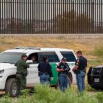 law enforcement officers confer beside patrol vehicles near a border fence