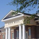 Ex-Mayor Admits China Ties — City Slams Doors Exterior view of a city hall building with columns and a clear blue sky
